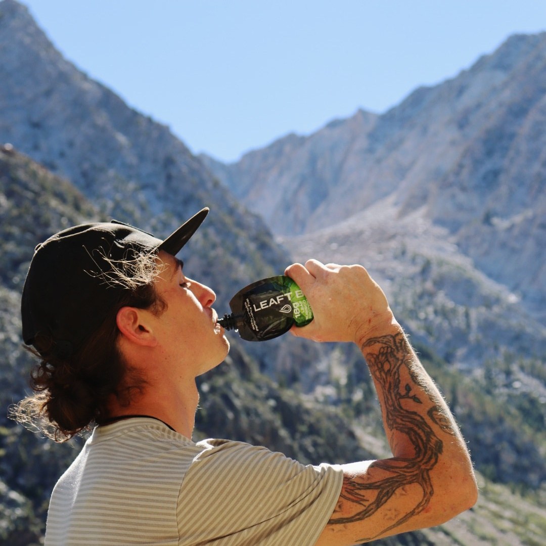Outdoor adventurer drinking Leaft Blade protein fuel with rugged mountains in the background.